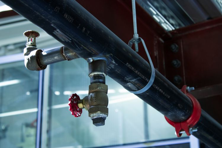 Overhead steel pipework with brass valves and red handwheels inside a commercial building