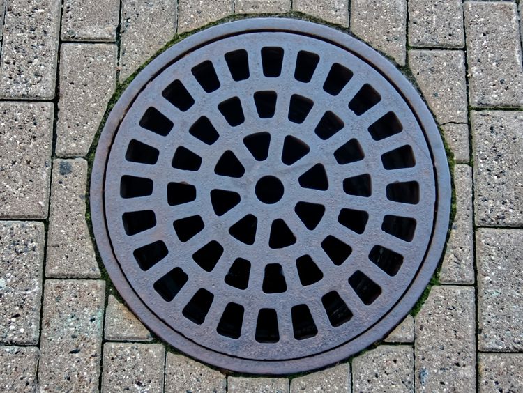 A round cast-iron drain cover set into brick paving