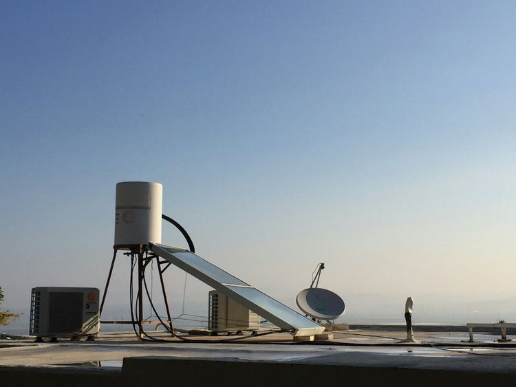 A solar geyser on its stand on a flat roof against a clear sky
