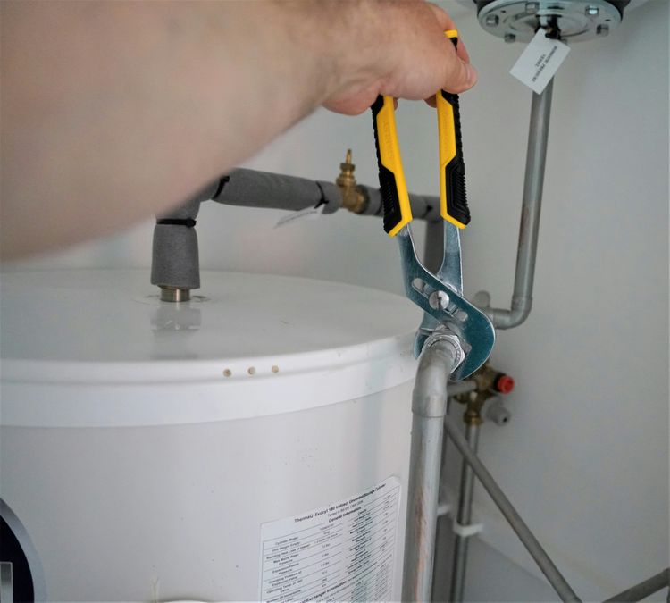 Plumber tightening a fitting on top of a hot water cylinder with grips