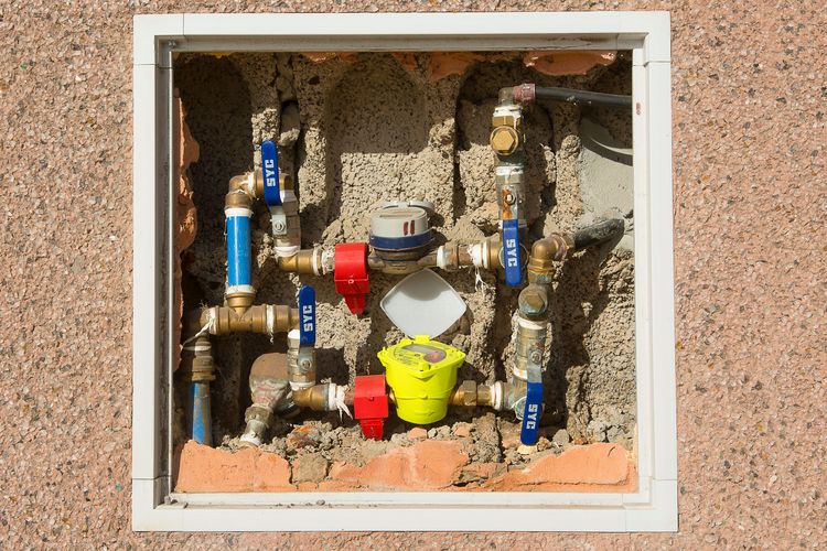 A water meter box with brass valves and the meter set into a wall