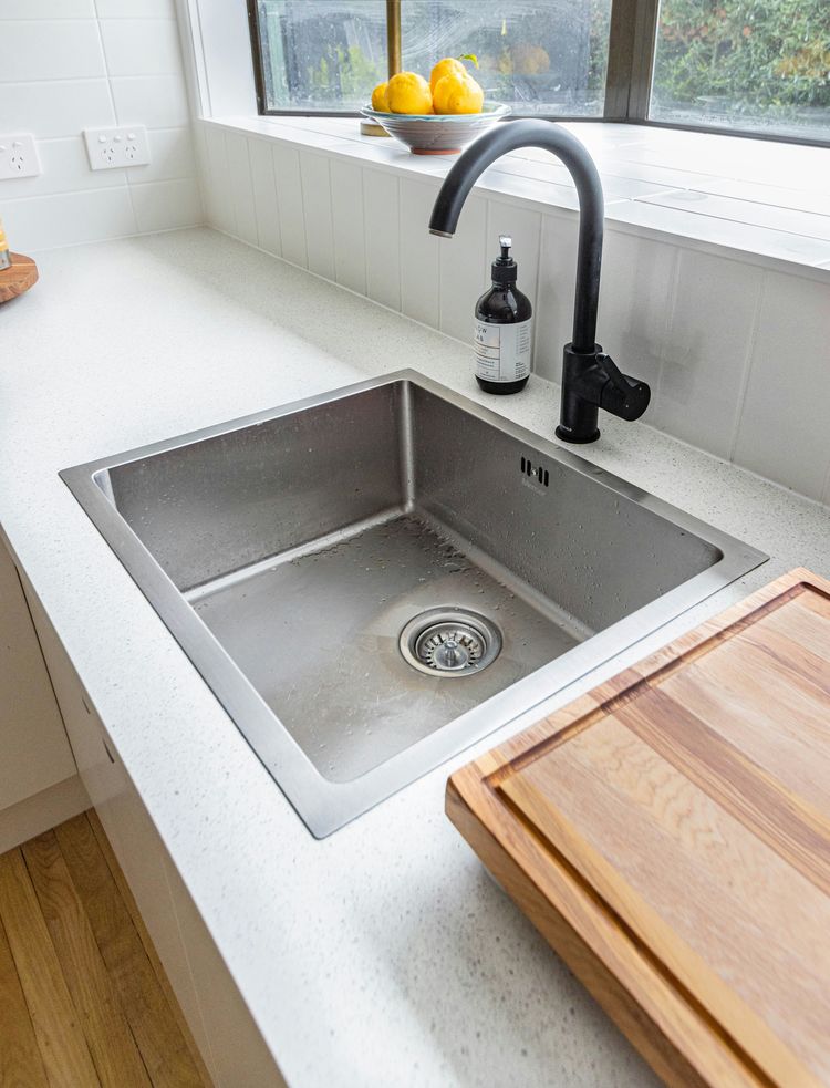 A stainless steel kitchen sink with a black gooseneck mixer tap