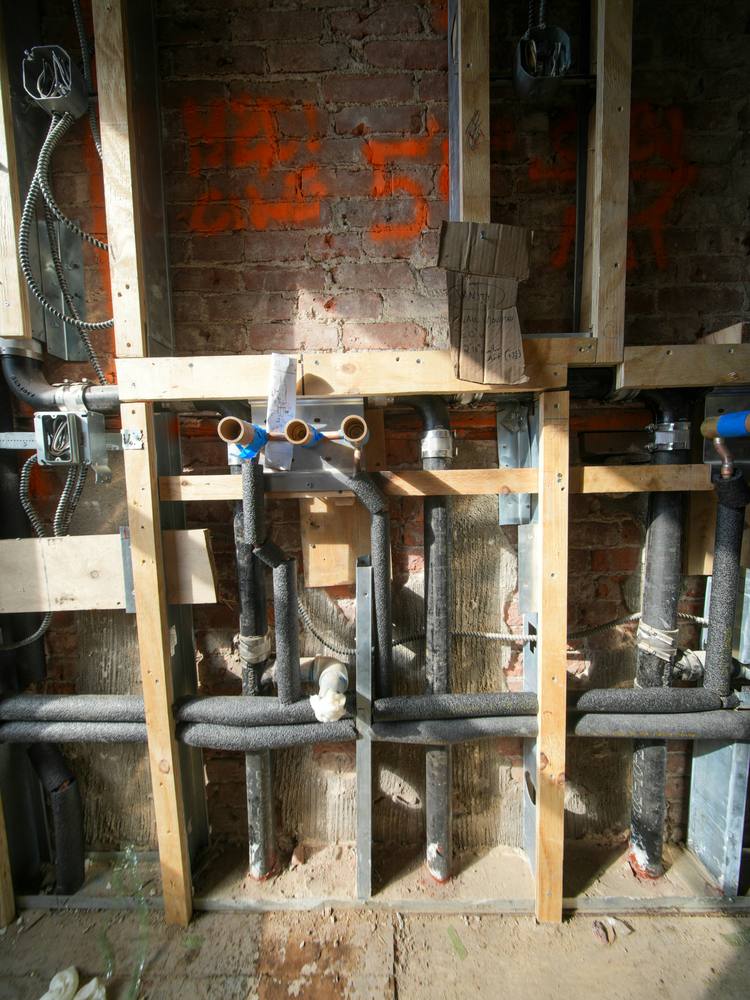 Insulated water pipes and fittings inside an open timber-framed wall on a building site