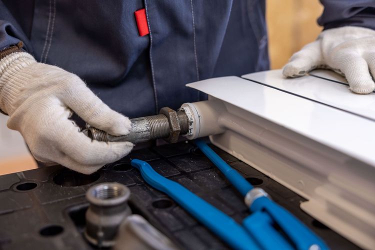 Gloved hands fitting a threaded steel pipe connection on a workbench