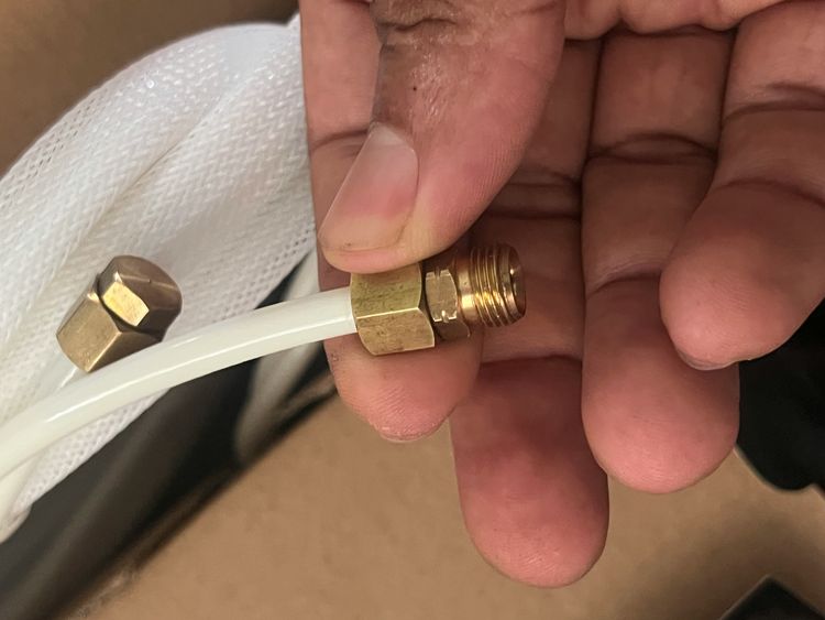 A hand holding a brass fitting pushed onto white plastic pipe