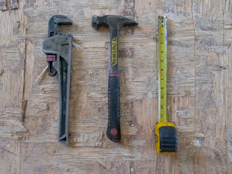 Pipe wrench, claw hammer and tape measure laid out on a wooden floor