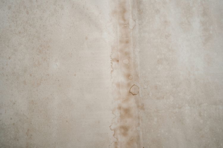 A brown water stain streaking down a pale plastered wall