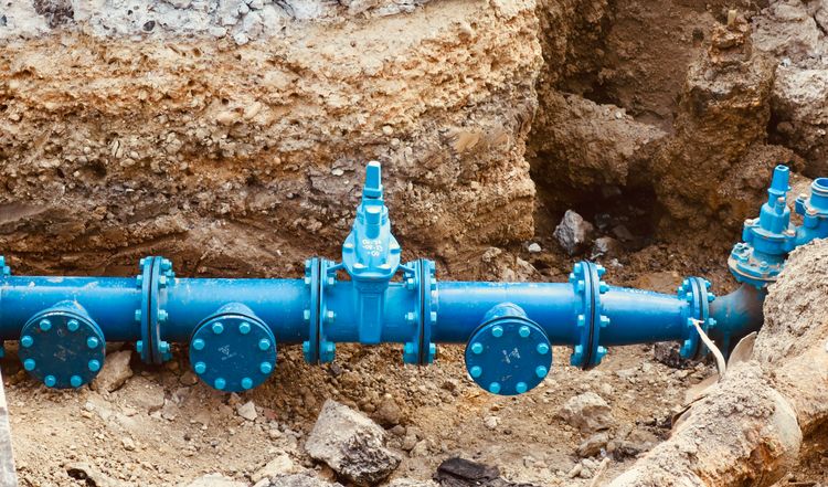 A blue water main with gate valves and flanged fittings in an open trench